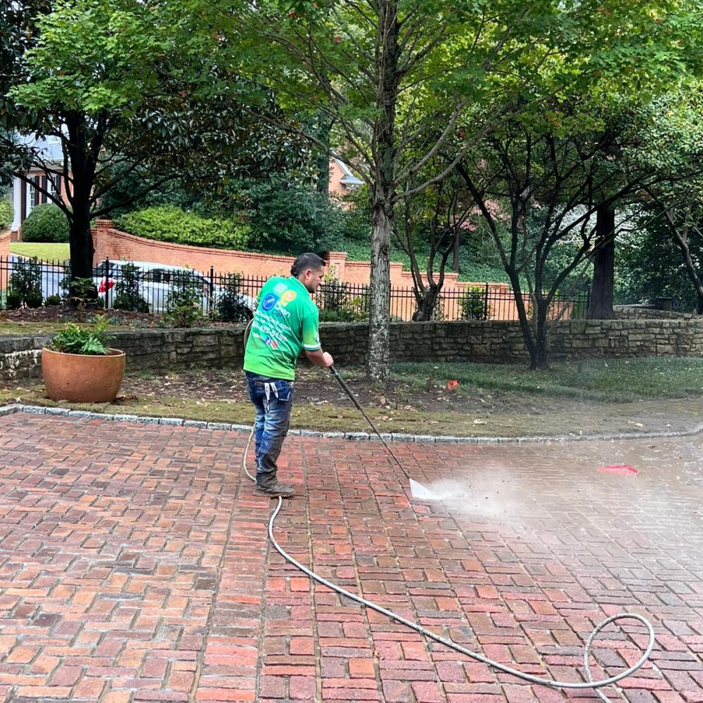 A JM Clean Care cleaning technician pressure washes a brick pathway.